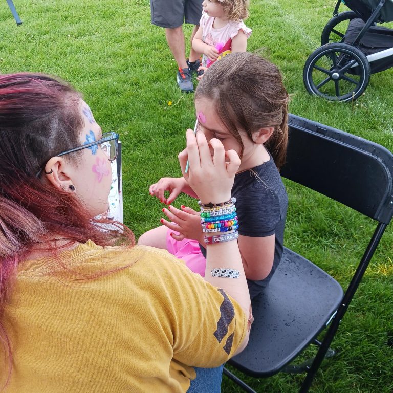 Bex face-painting a young girl in a black t-shirt